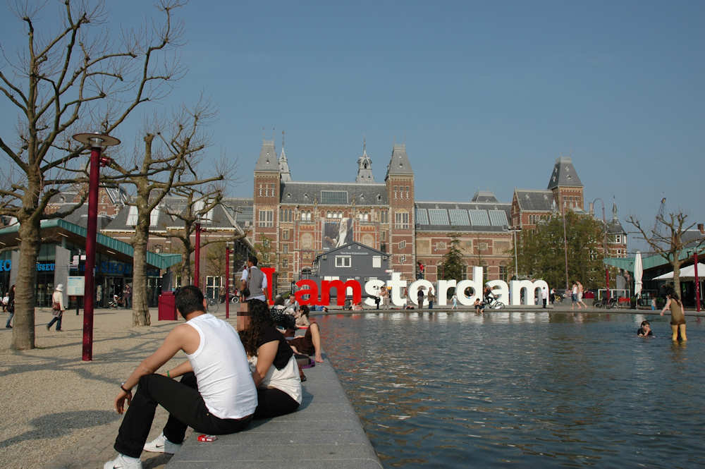 Folk koser seg i solen på Museumsplein foran Rijksmuseum i Amsterdam — Foto: Gaute Nordvik